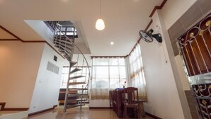 Une pièce spacieuse dotée d’un plancher ciré, d’un escalier en colimaçon, d’un coin repas avec des chaises et une table, et d’un ventilateur décoratif.