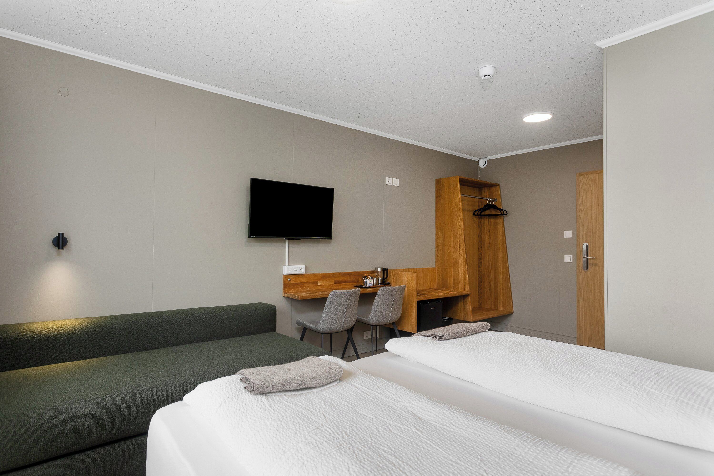 Ein Hotelzimmer mit einem Bett, einer Couch, einem Schreibtisch mit zwei Stühlen, einem Fernseher und einem Kleiderschrank.