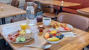 Een ontbijttafel met borden eieren, spek, toast en fruit, een waterfles, een glas sinaasappelsap en een kaars.