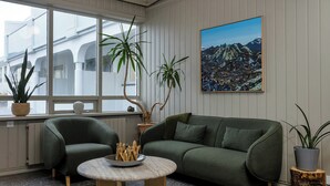Een moderne woonkamer met een groene bank, een ronde salontafel en twee potplanten.