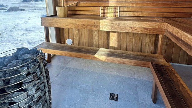 Een sauna met houten banken, een stenen wasbak en uitzicht op een besneeerd landschap.