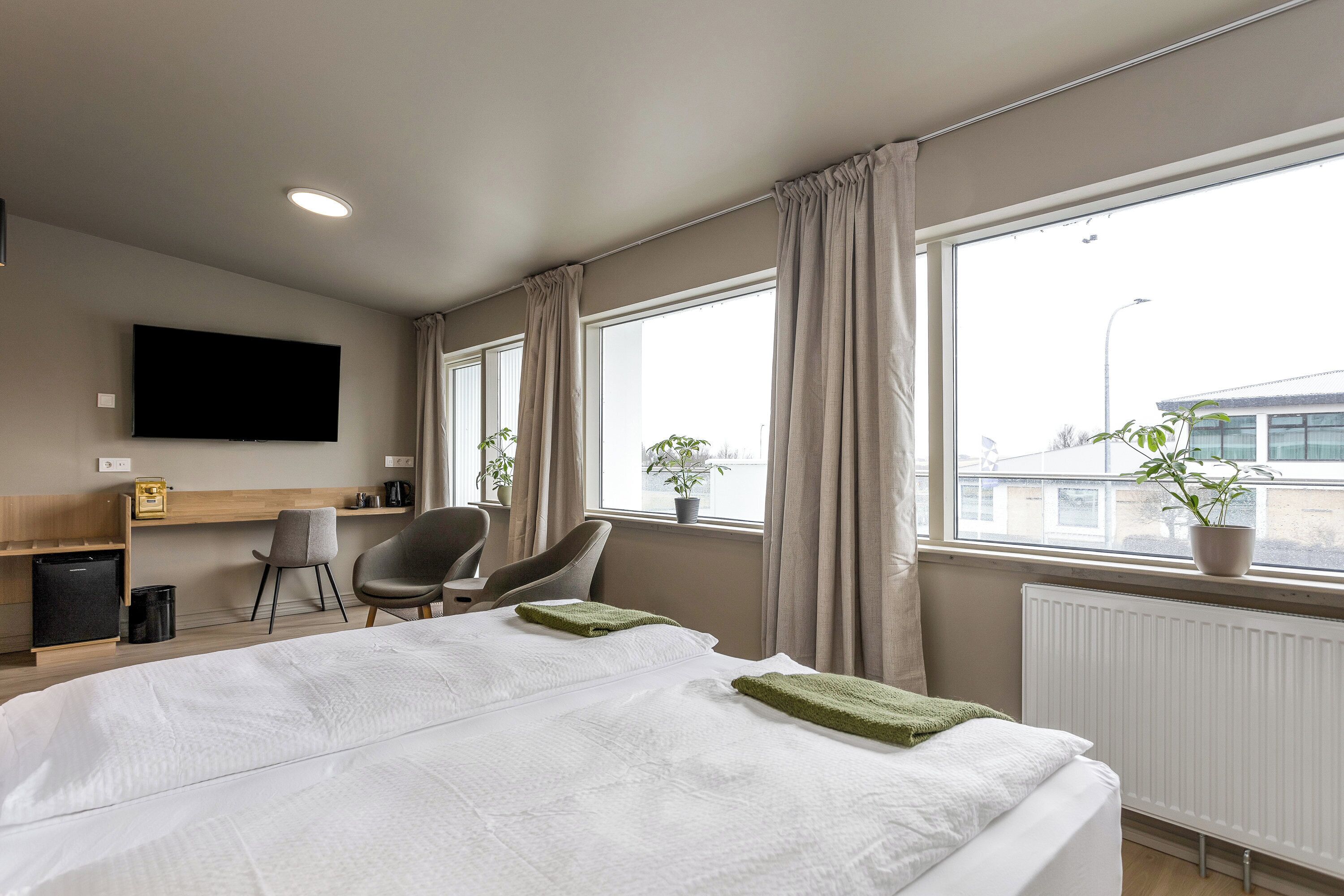 A hotel room with a bed, a desk, a chair, a television, and a window with curtains.