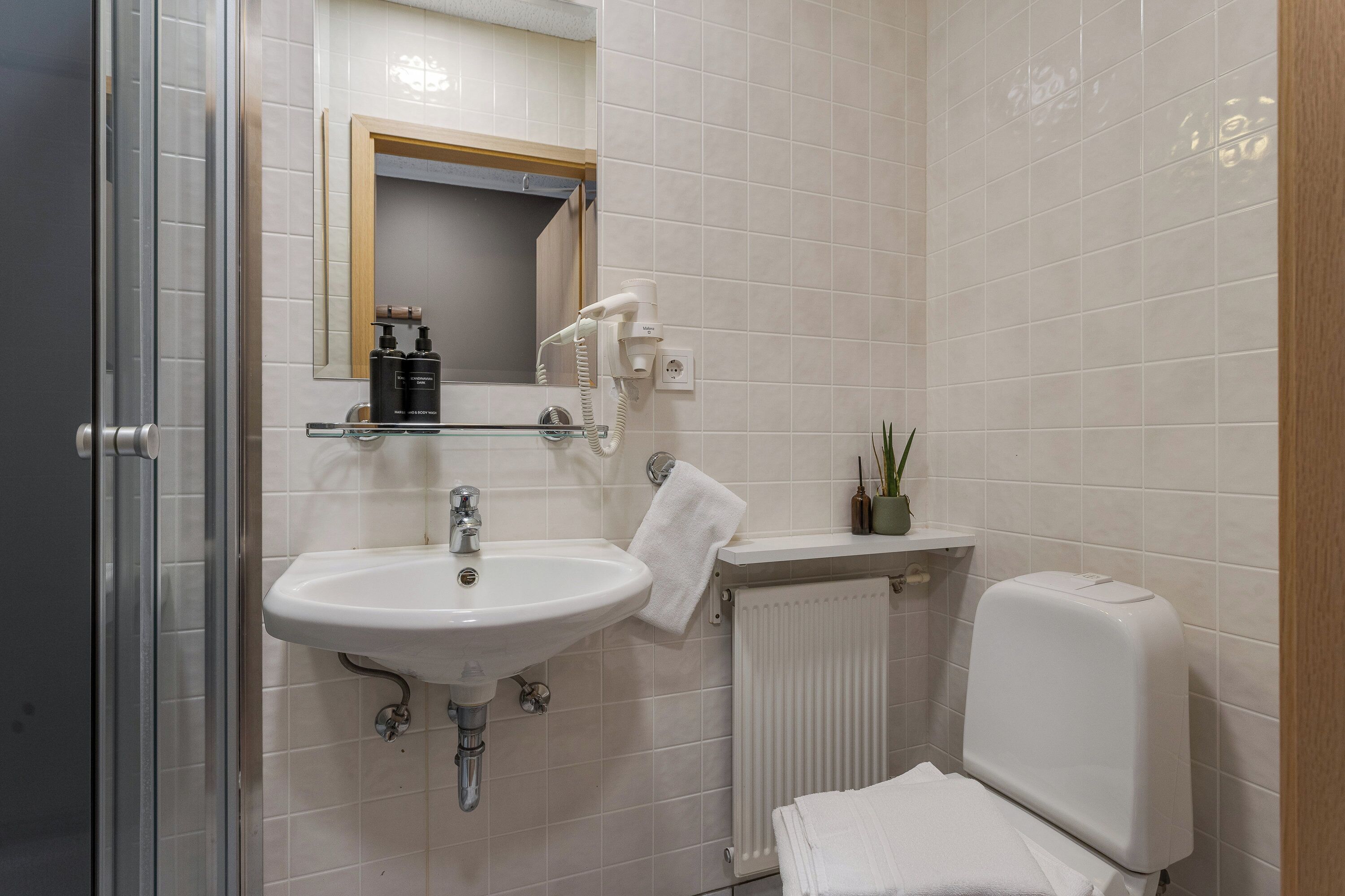 A bathroom with a sink, mirror, hairdryer, and a radiator.