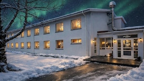 Hotel met meerdere verlichte ramen, een oprit bedekt met sneeuw en een uitzicht op de nachthemel met het noorderlicht.