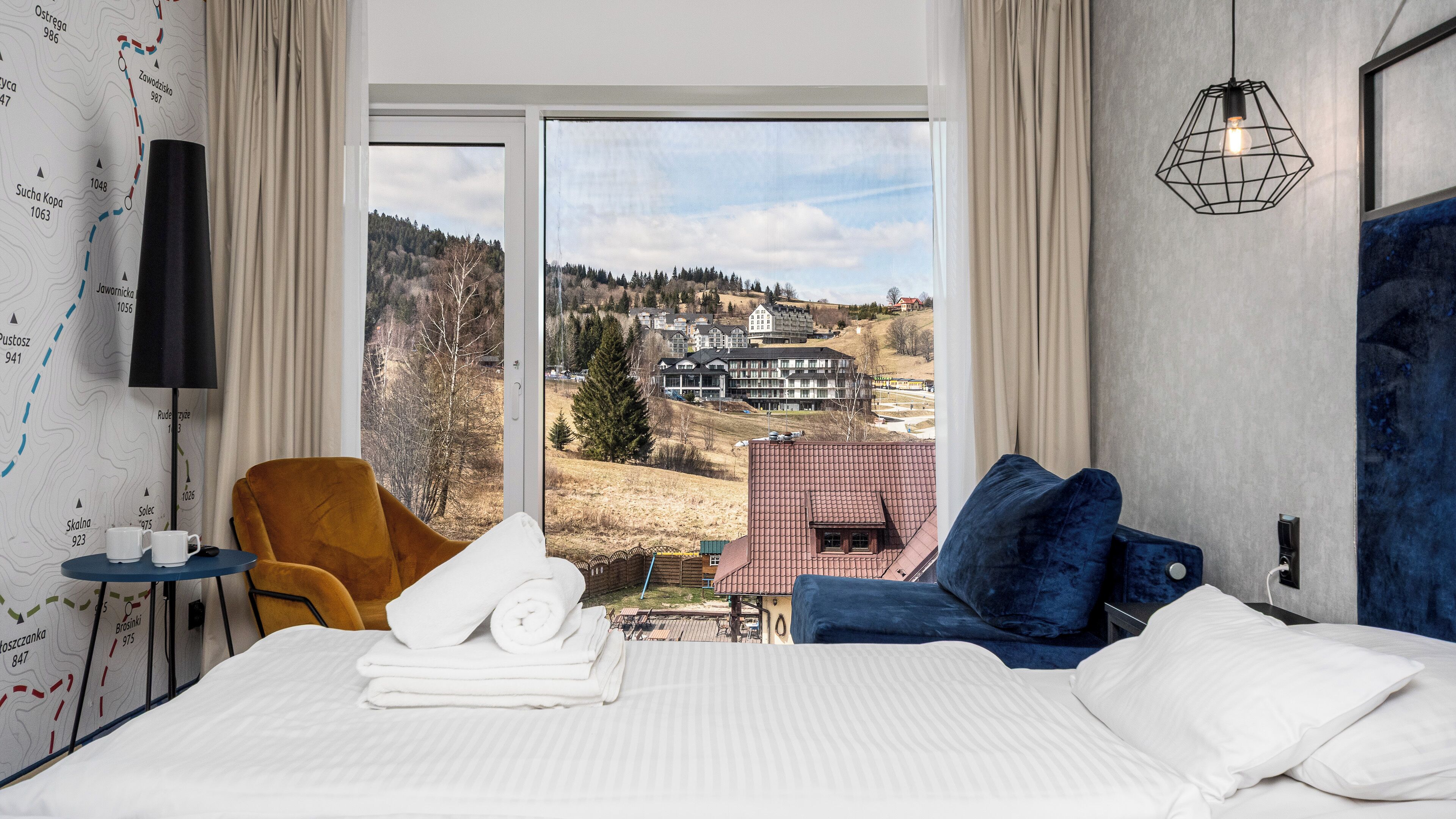 A hotel room with a large bed, a view of a village, a map on the wall, and a lamp.