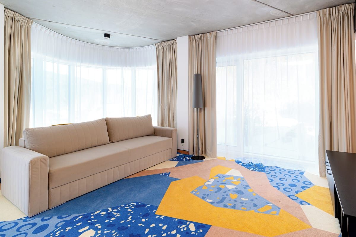 Une chambre d’hôtel moderne avec un canapé beige, un téléviseur à écran plat et une moquette aux couleurs vives.