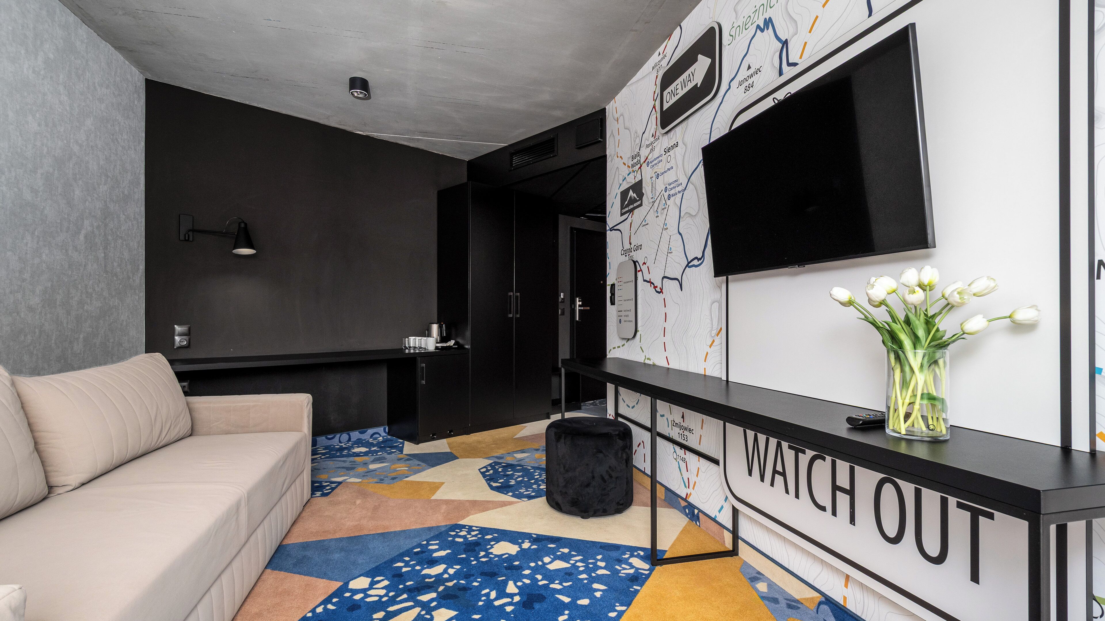 Un salón moderno con un sofá, una mesita de centro, un televisor montado en la pared y un jarrón decorativo con flores.