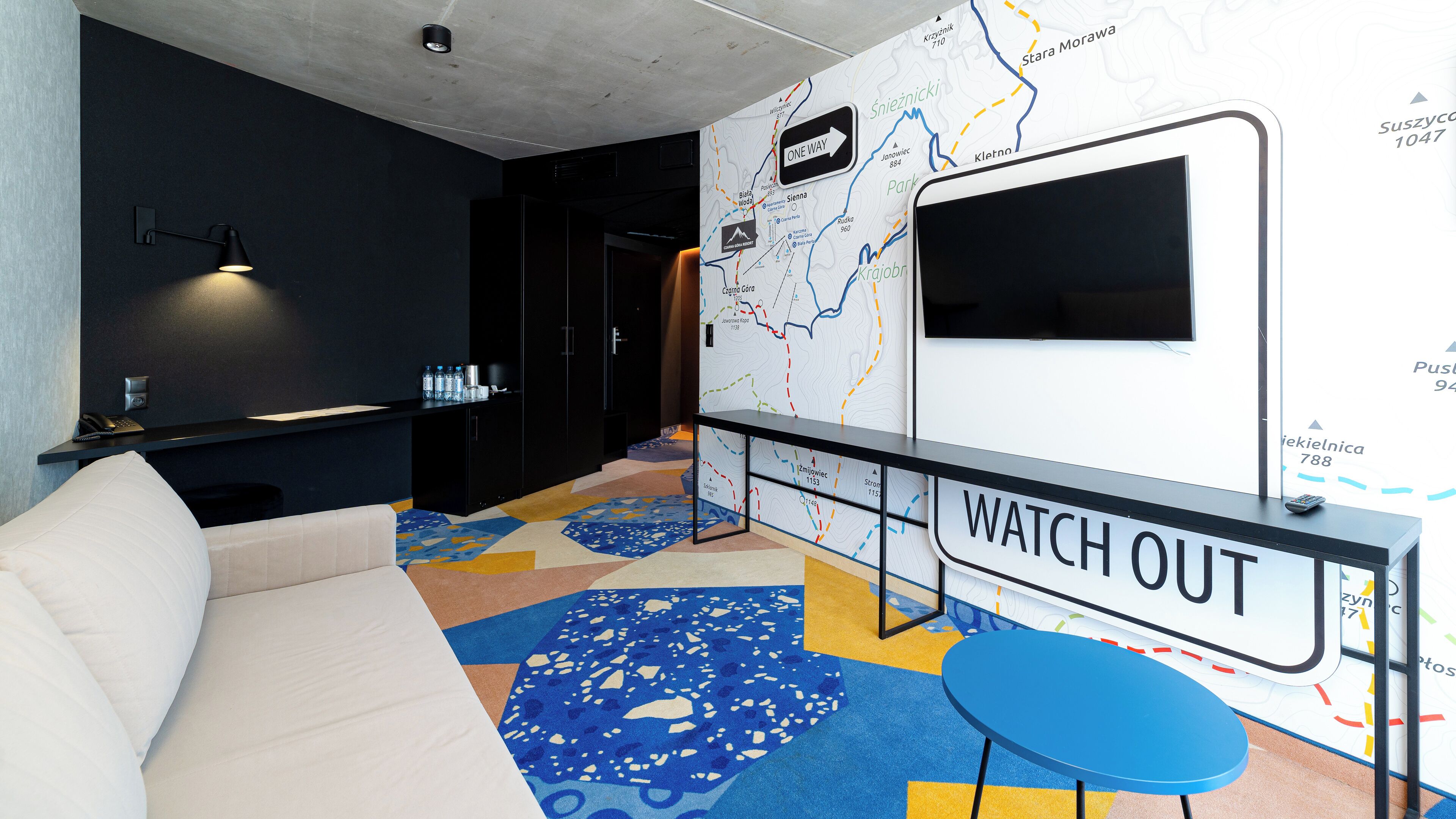 Un moderno vestíbulo de hotel con un sofá, una pequeña mesa, un mural de mapa y una pantalla de televisión.