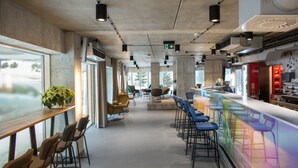 Un café moderno con una barra larga, taburetes y una zona de estar con sillas y mesas.