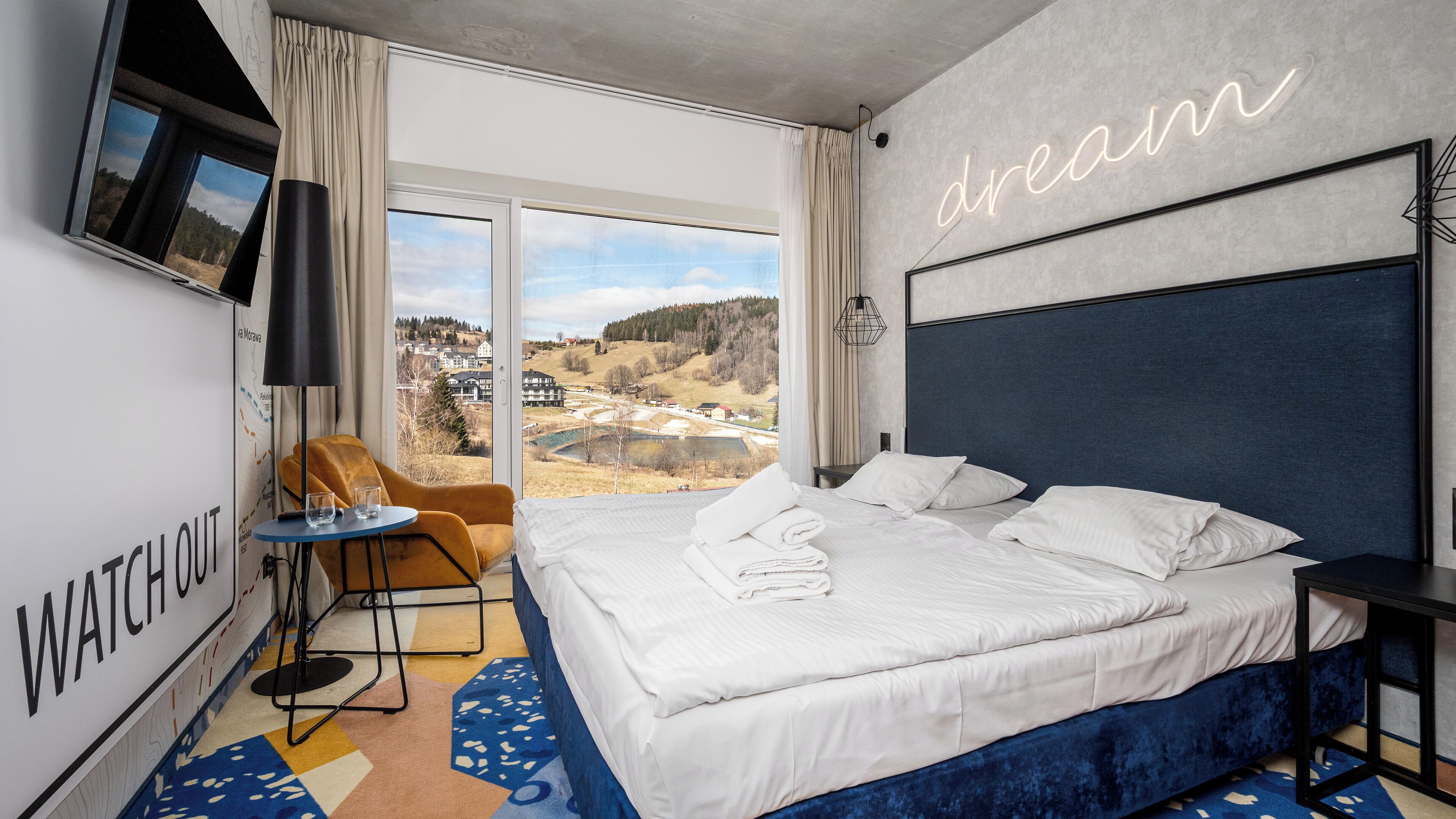 Ein Hotelzimmer mit einem großen Bett, einem an der Wand befestigten Fernseher, Blick auf die Landschaft und einem Schild mit der Aufschrift 'dream'.