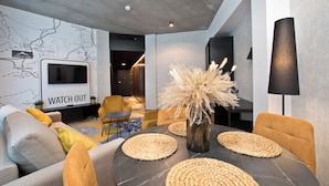 Una sala moderna con un mapa en la pared, una zona de comedor con individuales tejidos y un jarrón grande con plumas de pampa.