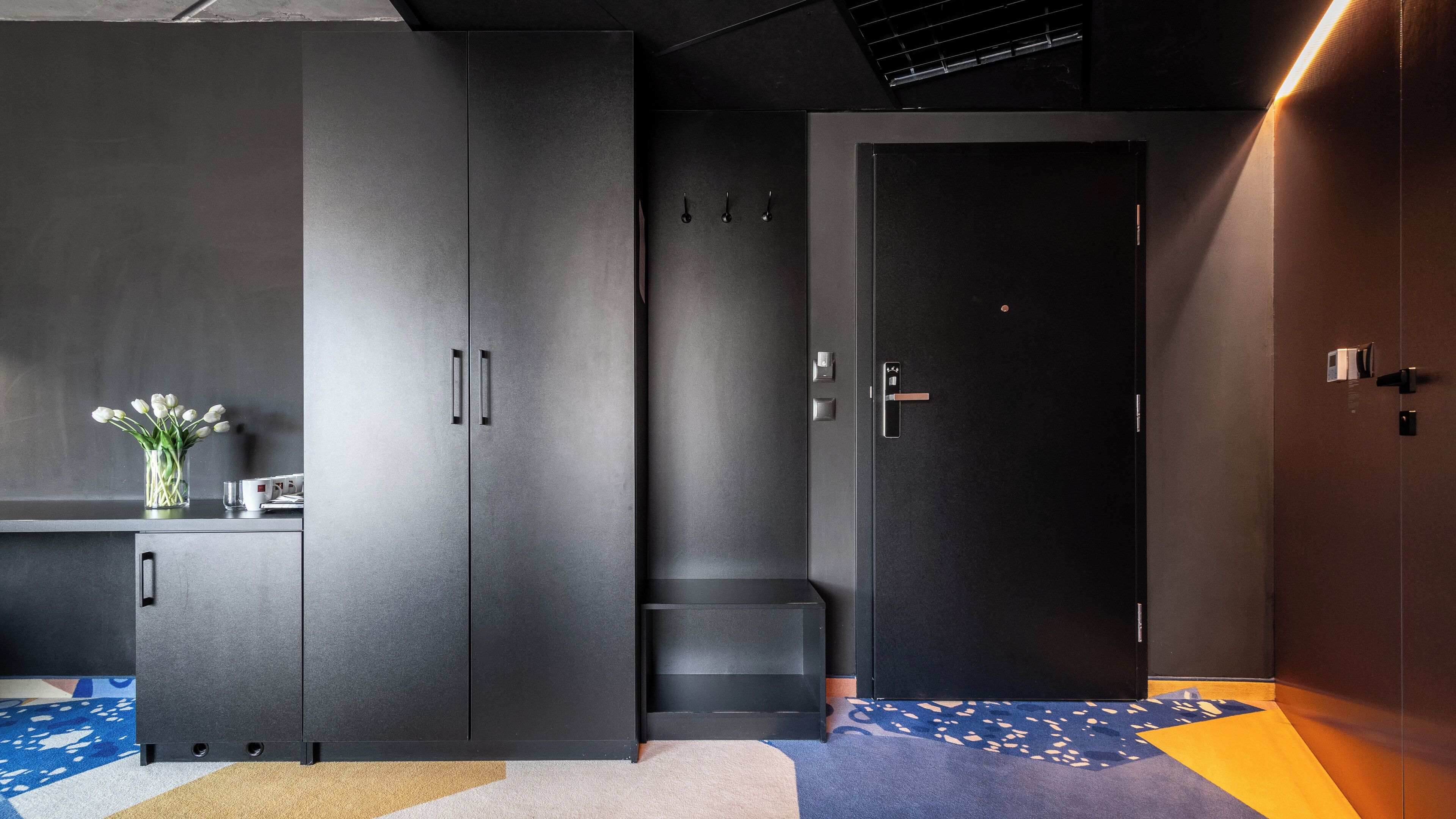 A modern, dark-themed room with a large wardrobe, a small seating area, and a door with a handle.