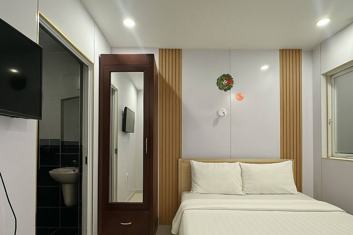 A hotel room with a bed, a TV mounted on the wall, a wooden door, and a bathroom visible through an open door.
