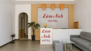 A modern hotel lobby with a reception desk, a potted plant, a sofa, and a fan. - Lam Anh Hotel (Xuan Huong - Da Lat)