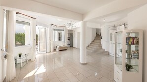 A spacious, modern interior with a high ceiling, a staircase, and a glass display cabinet.