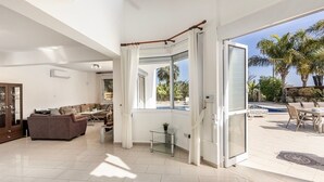 A spacious living area with a large sliding glass door leading to an outdoor patio with a pool and palm trees.