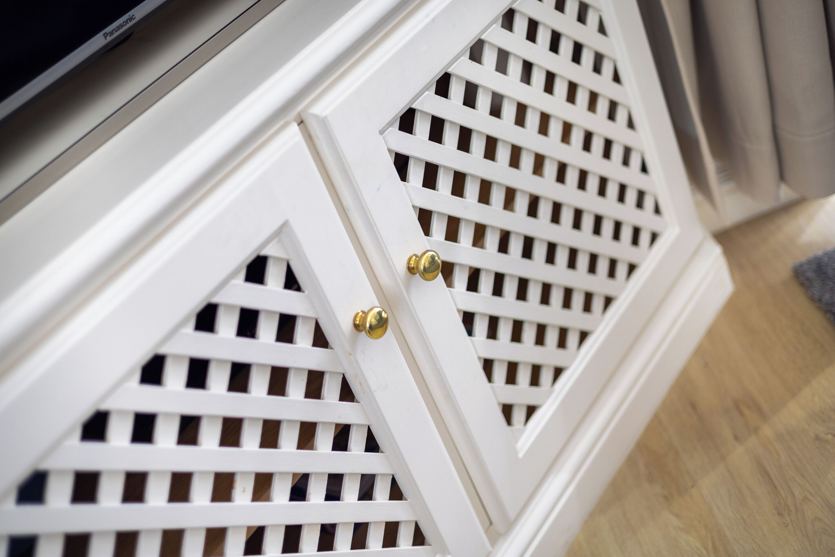 A white cabinet with a geometric lattice design and brass handles.