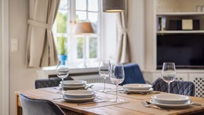 A dining table set with plates, glasses, and cutlery, with a lamp above and a bookshelf in the background. - Gaat 7 - Wohnen im Historischen Ortskern Keitum (Sylt / OT Keitum)