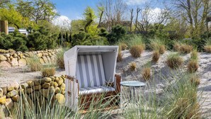 A beach chair with a striped cushion, a small round table, and a stone wall in a natural setting with sand and sparse vegetation. - Gaat 7 - Wohnen im Historischen Ortskern Keitum (Sylt / OT Keitum)