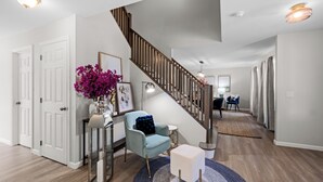 A modern interior with a wooden staircase, a blue armchair, a white ottoman, and a decorative mirror.