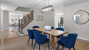 A dining area with a wooden table, blue chairs, and a modern pendant light. - Last Minute Deal ! New Construction 3 blocks to Boone St. and walkable to ocean wall (Narragansett)