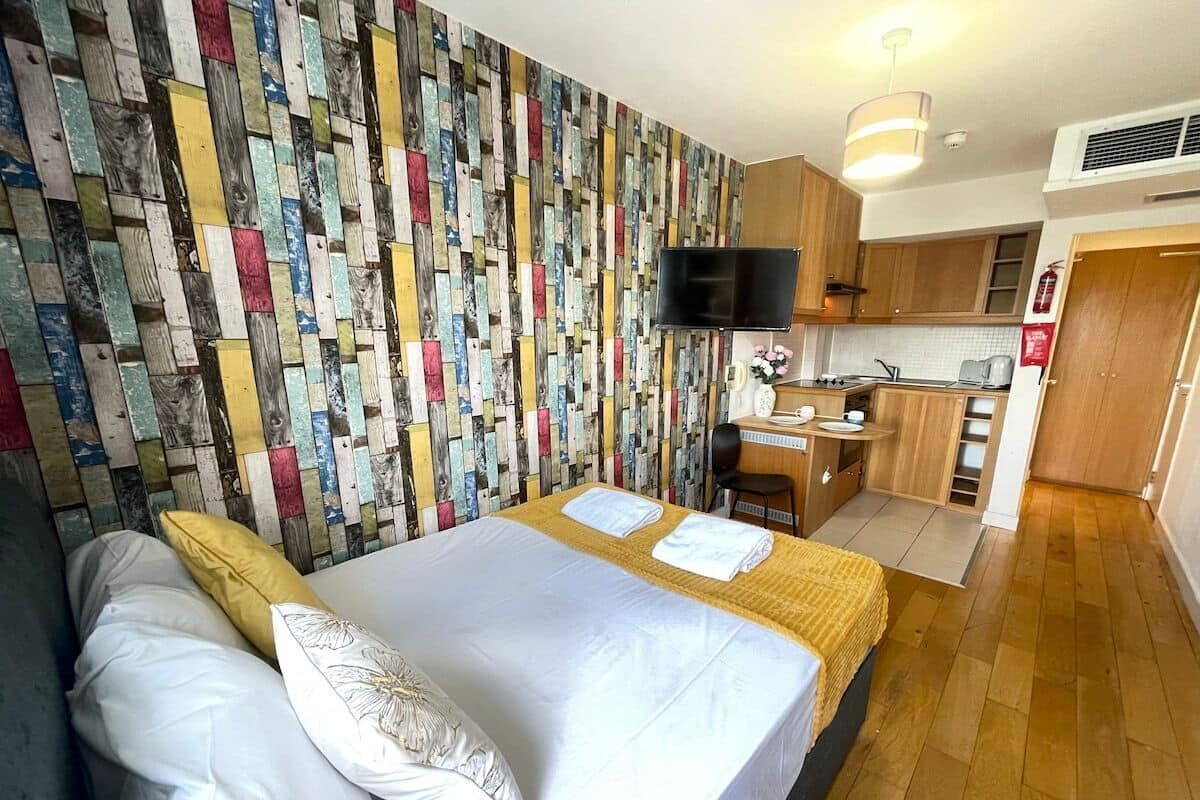 A hotel room with a bed, a desk, and a kitchenette.