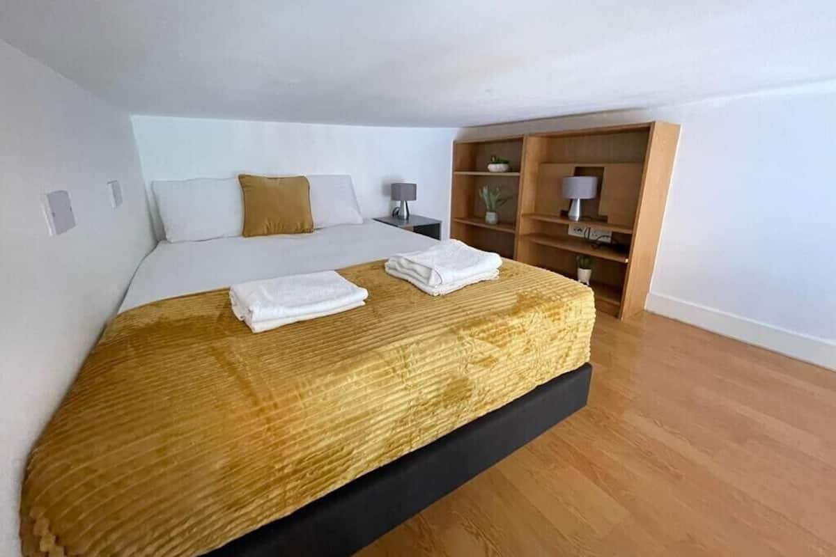 A modern bedroom with a large bed, a wooden headboard, a nightstand, a lamp, and a built-in shelf unit.