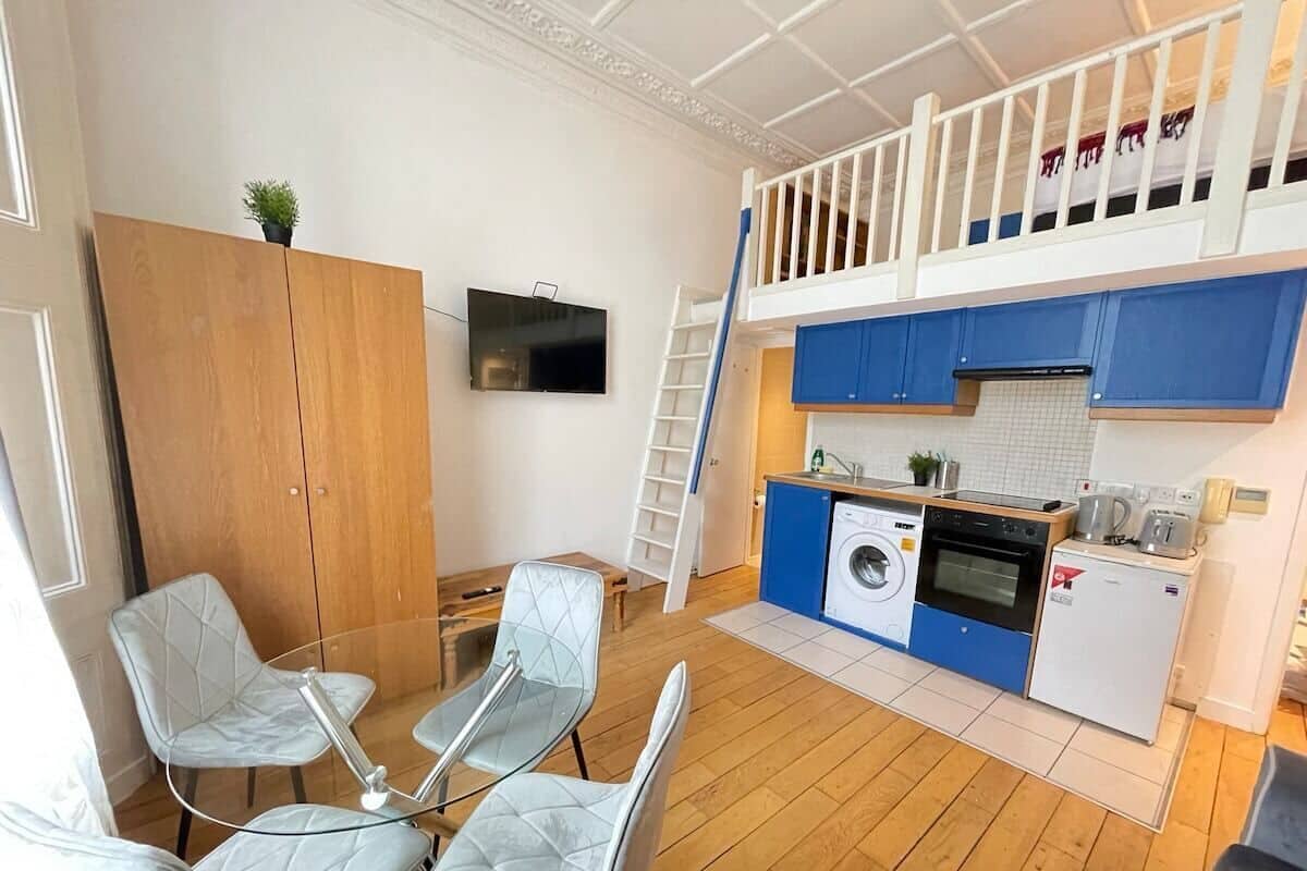 A compact living space with a kitchenette, a dining area with four chairs, a washing machine, and a small refrigerator.