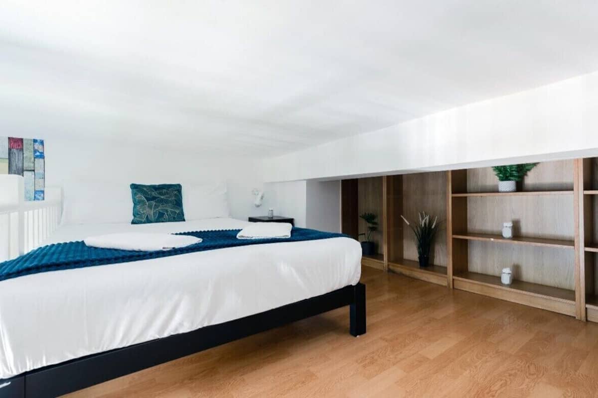 A modern bedroom with a bed, bedside tables, a wooden shelf unit, and a white radiator.