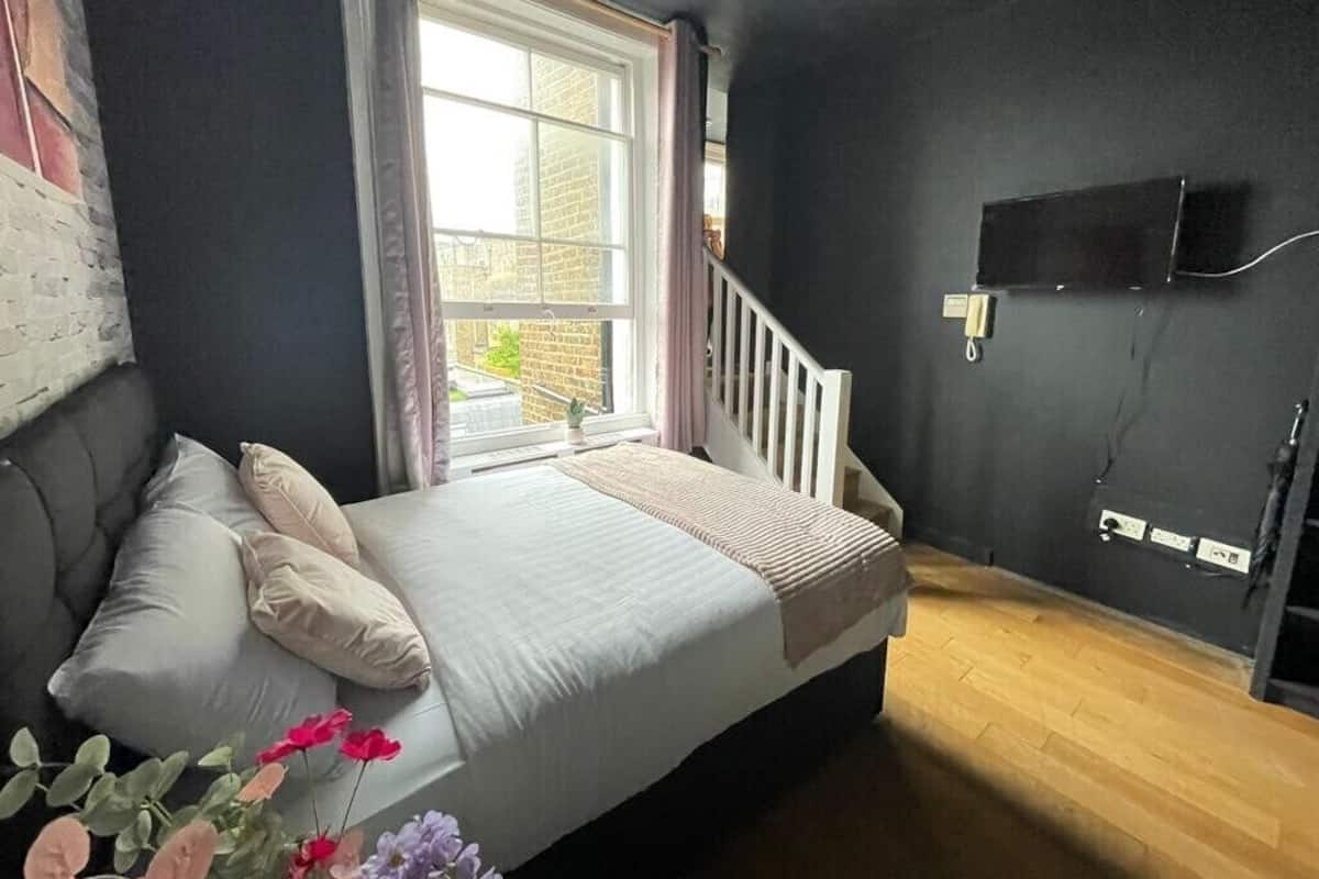 A bedroom with a bed, a window, a staircase, and a wall-mounted TV.