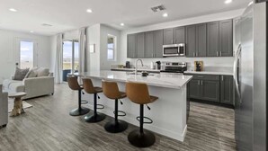 A modern kitchen with a central island, bar stools, and a refrigerator. - Stargazer - Hot tub, fire pit & deck (Page)