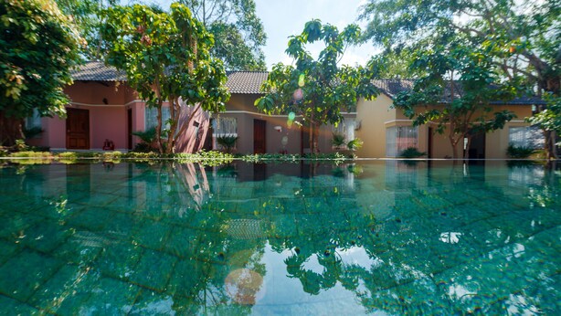 A clear swimming pool surrounded by trees and buildings with a tiled roof. - Phuc Thang Resort  (Phu Quoc)