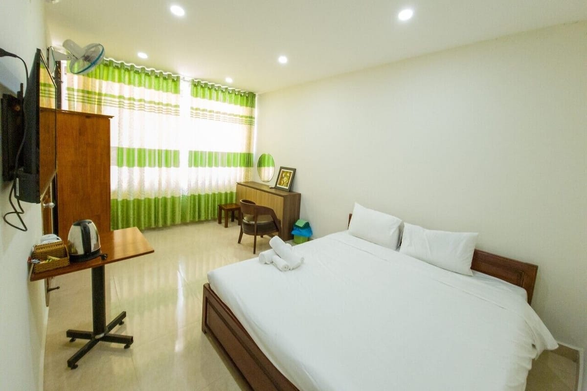 A hotel room with a bed, a desk, a chair, a wardrobe, and a window with curtains.