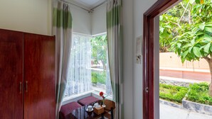 A room with a wooden wardrobe, a bench, a table with a vase and a basket, and a window with sheer curtains. - Phuc Thang Resort  (Phu Quoc)