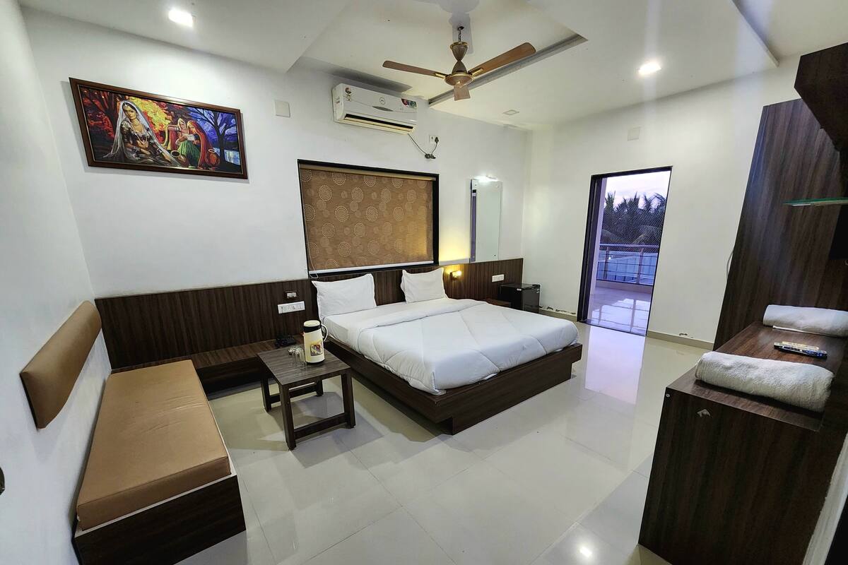 A modern hotel room with a large bed, a sofa, a small table, and a ceiling fan.