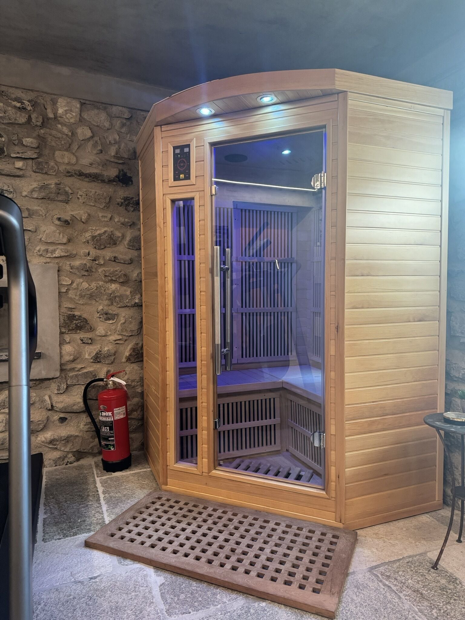 Eine Sauna mit Holzfassade, einer Glastür und einem Feuerlöscher in der Nähe.