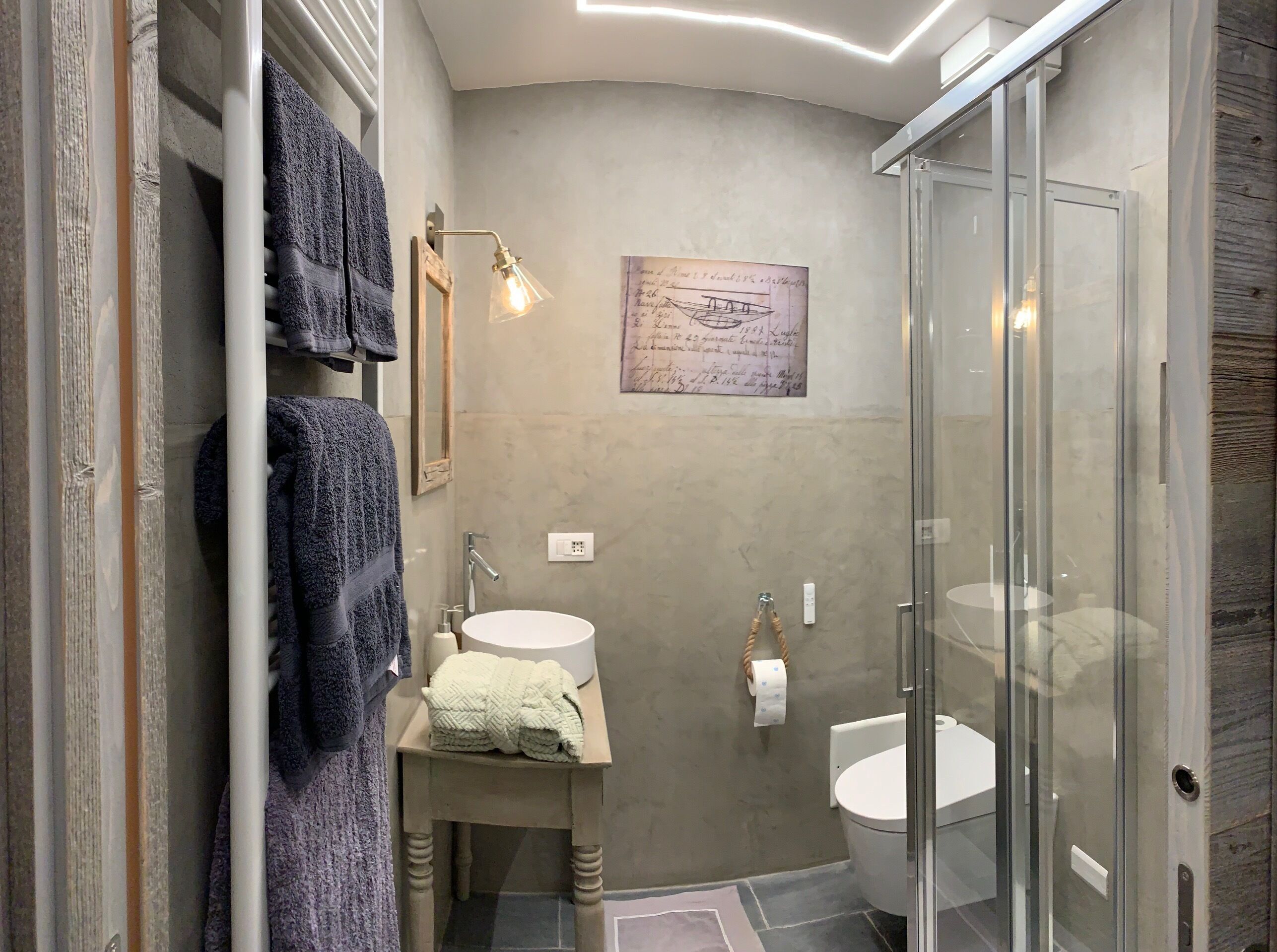 Une salle de bain moderne avec une douche à parois de verre, un lavabo avec une serviette et un luminaire fixé au mur.