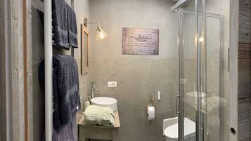 A modern bathroom with a glass shower enclosure, a sink with a towel, and a wall-mounted light fixture.