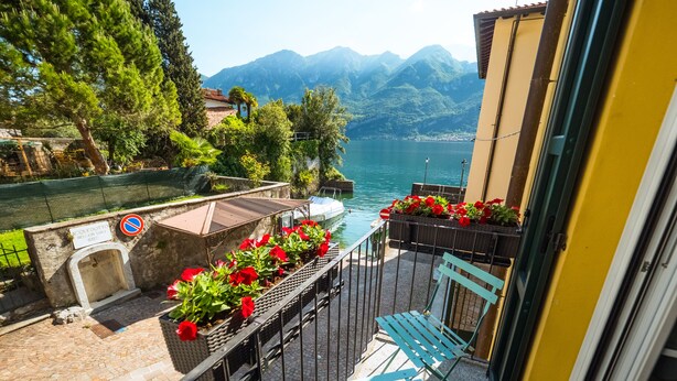 A balcony with a view of a lake and mountains, a no parking sign, and a bench with red flowers. - Al Molo 5 Apartments (Oliveto Lario)