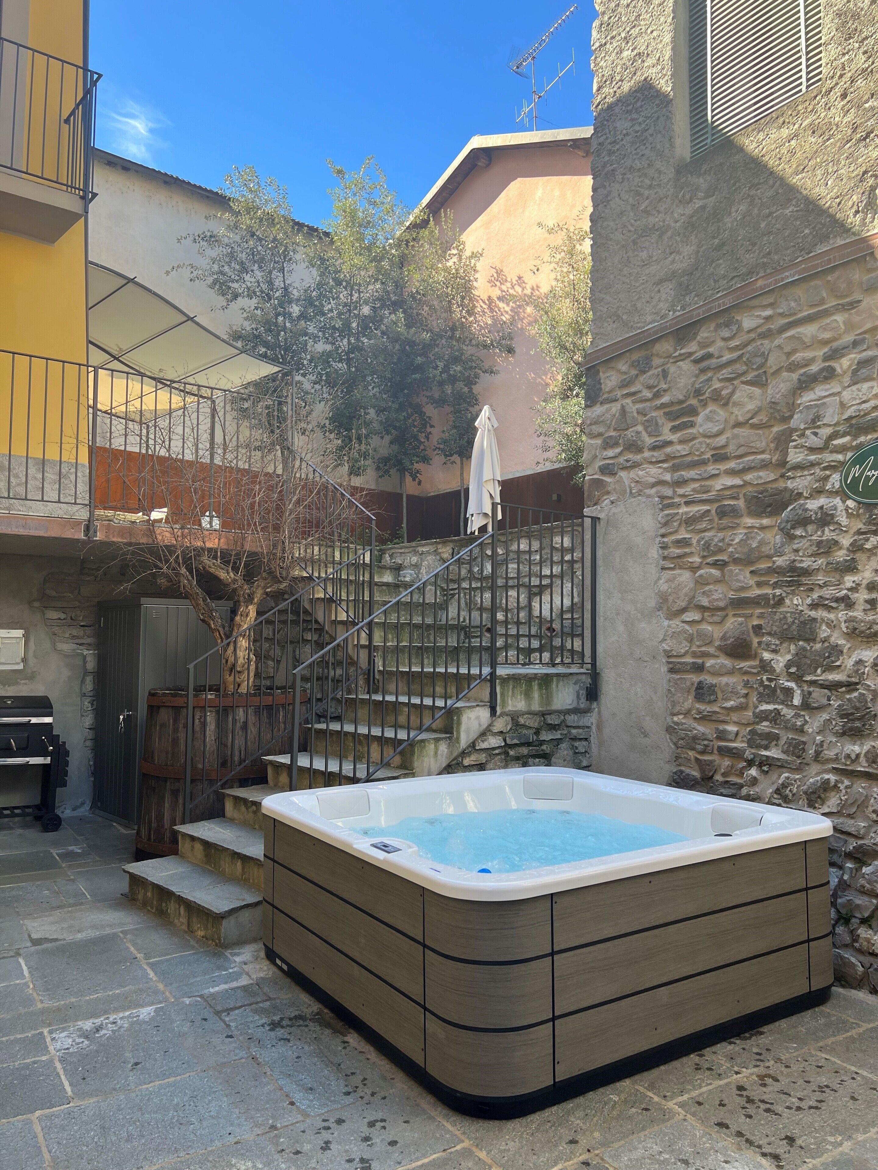 A hot tub in a courtyard with stone steps leading up to a balcony.