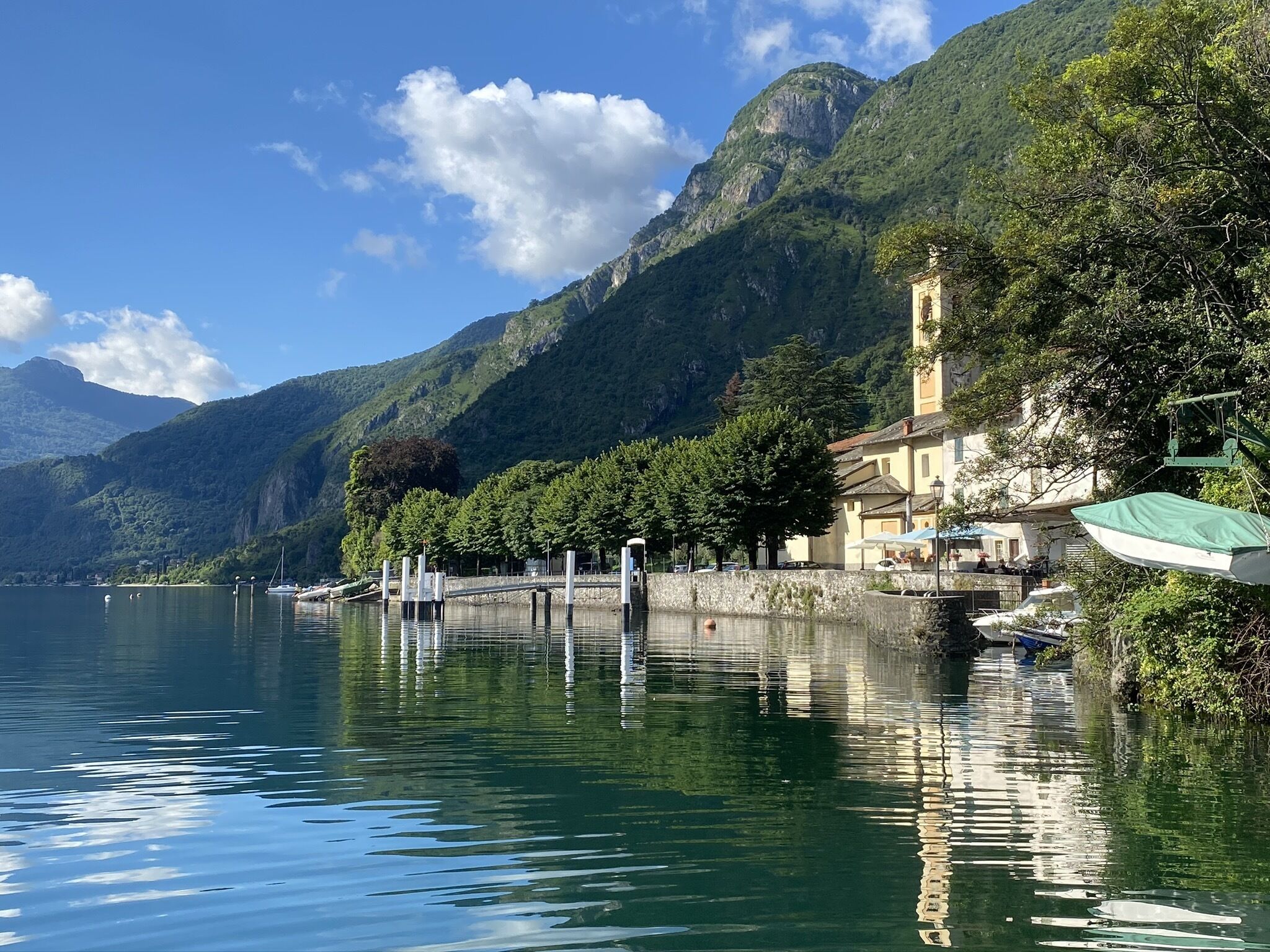Vista su un lago con montagne sullo sfondo, un molo con barche e un edificio con tenda verde.