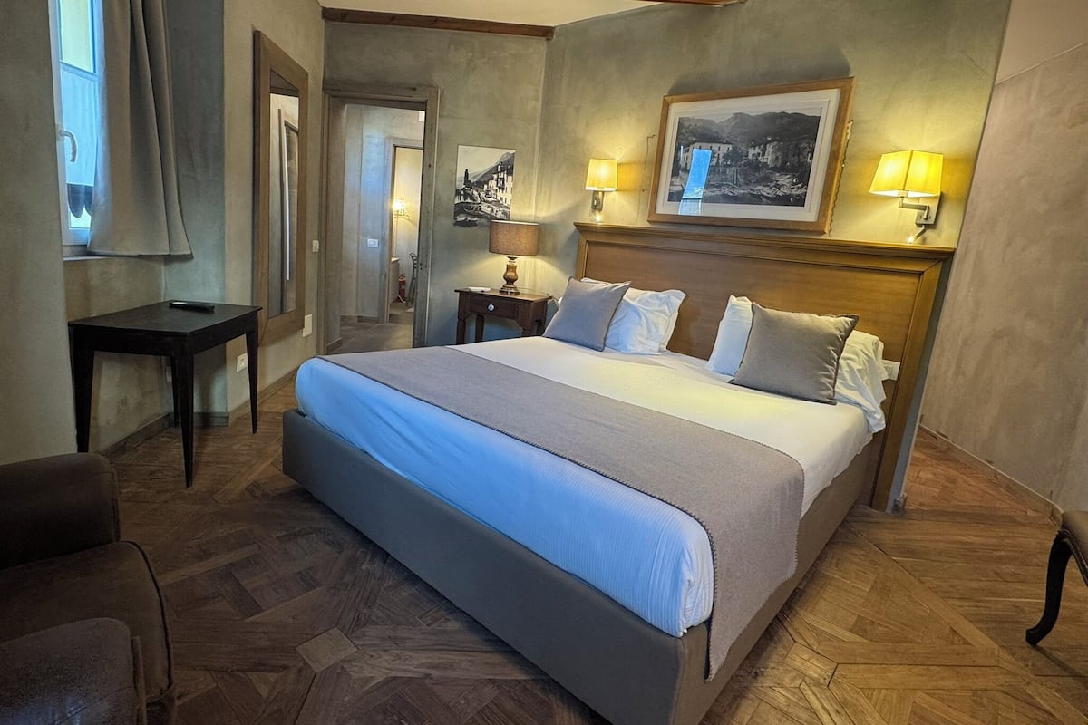 A hotel room with a large bed, two bedside lamps, a framed picture on the wall, and a small table.