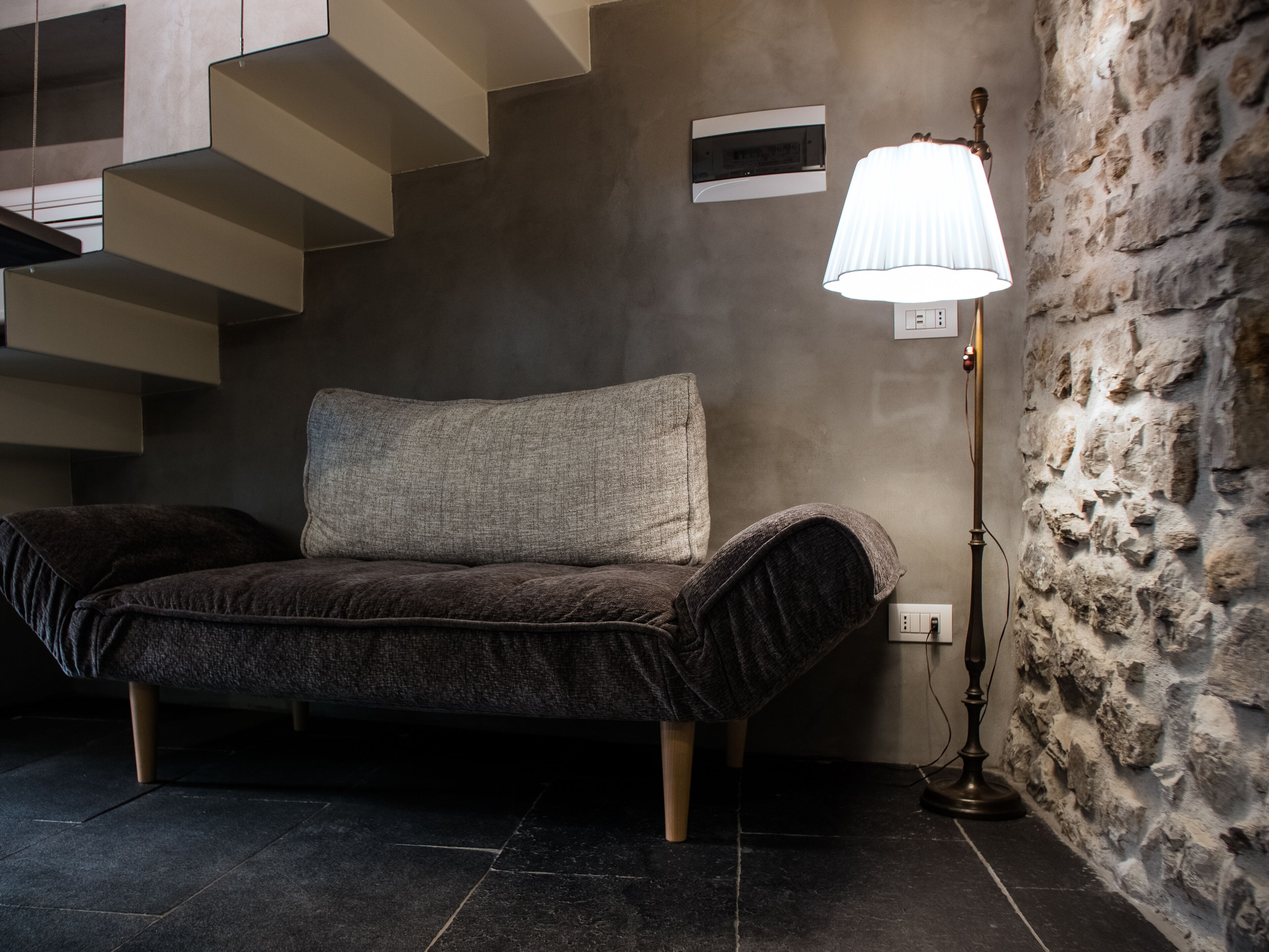 A modern living room with a sofa, a lamp, and a stone wall.