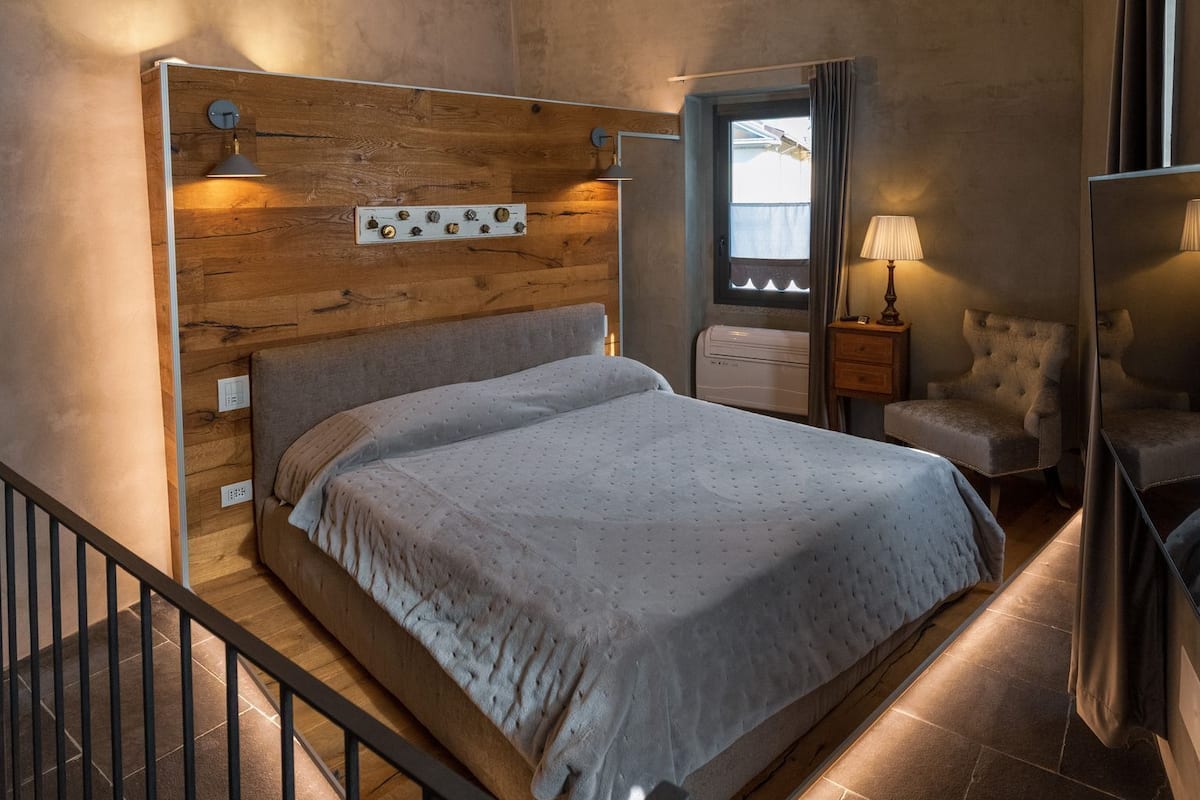 A bedroom with a wooden headboard, a bed with a grey duvet, a nightstand, a chair, and a window with curtains.