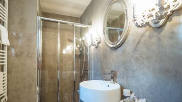 A bathroom with a glass-enclosed shower, a round sink, and a mirror with ornate detailing.