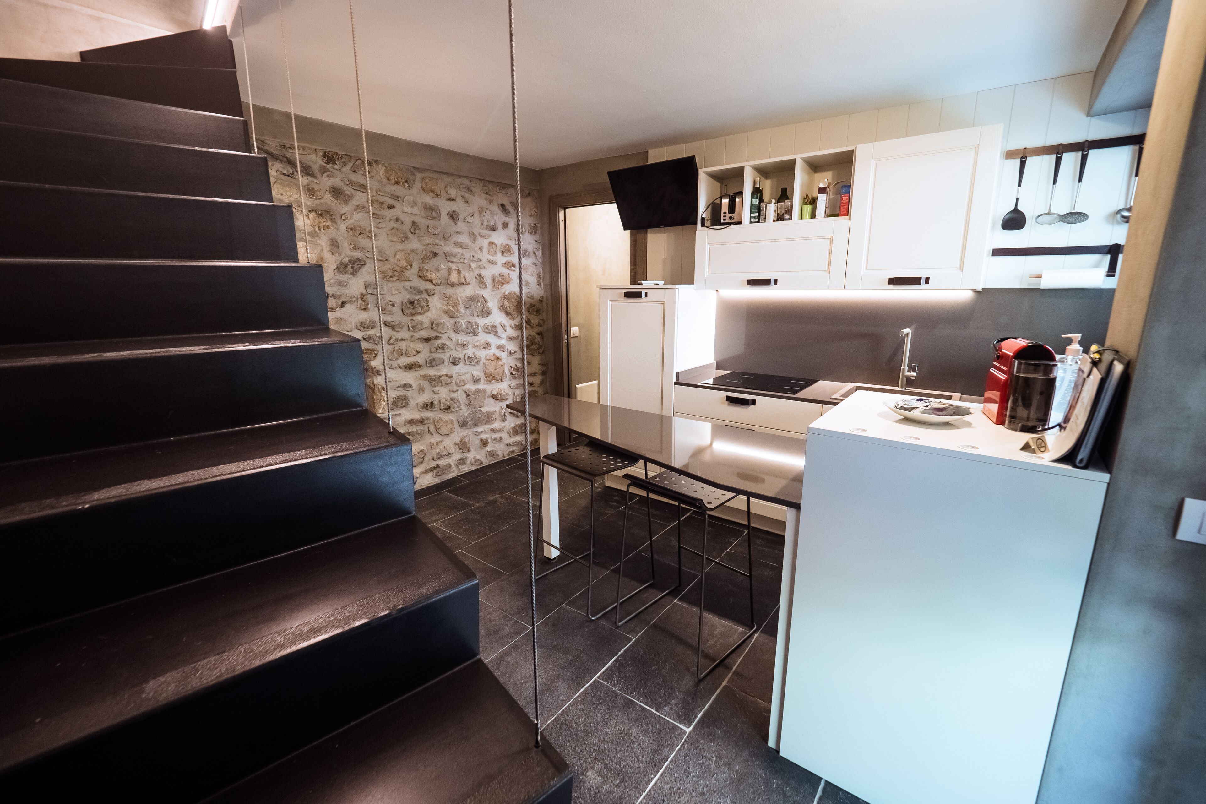 Une cuisine moderne dotée d’une cuisinière intégrée, de meubles blancs et d’un mur en pierre.