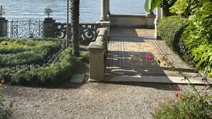 A garden pathway leading to a view of a lake with mountains in the background, surrounded by lush greenery and a decorative archway. - Al Molo 5 Apartments (Oliveto Lario)