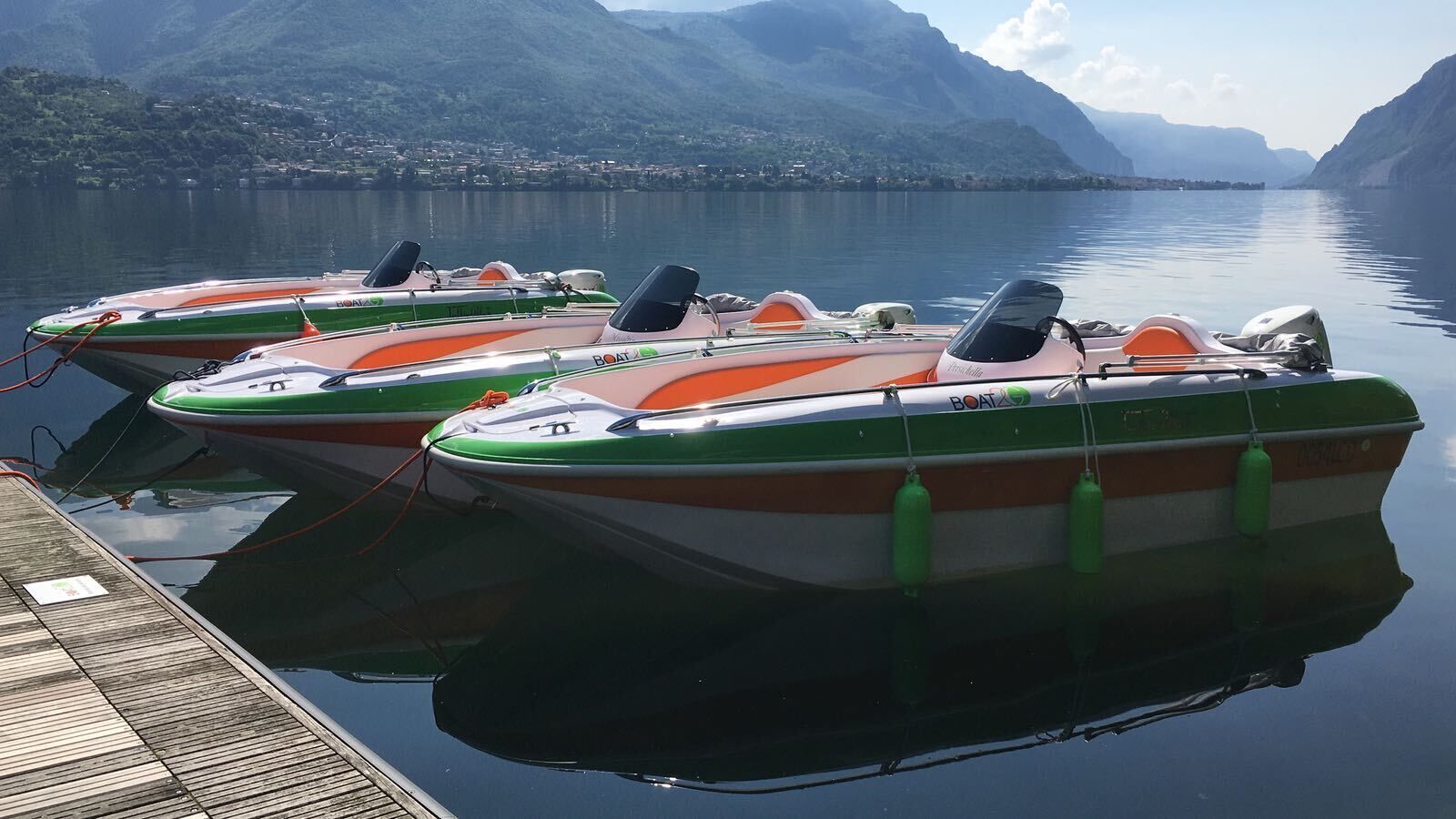 Tre motoscafi ormeggiati a un molo con montagne sullo sfondo.