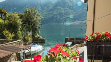 Un balcón con flores rojas, vista a un lago y montañas al fondo.