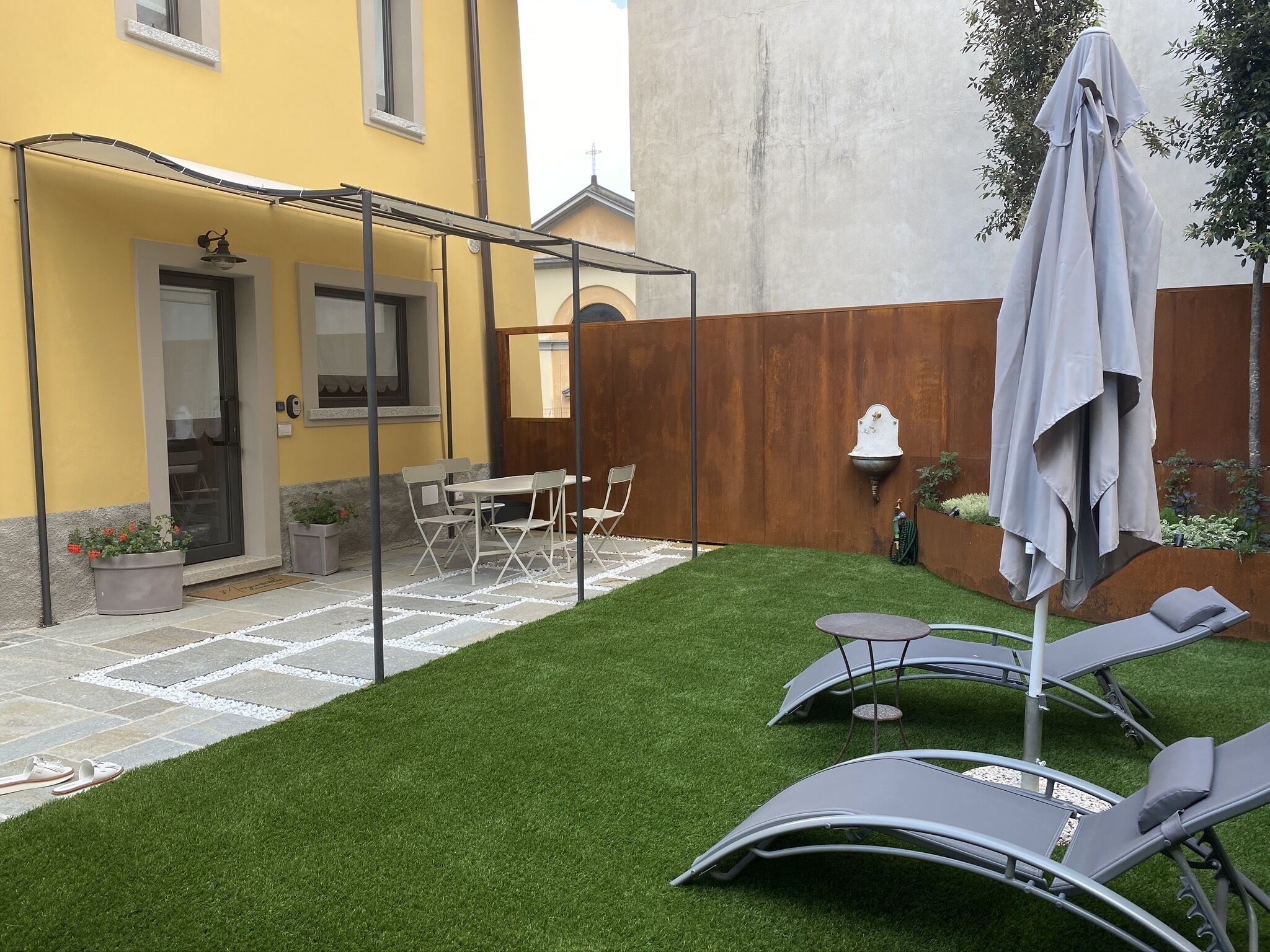 A courtyard with artificial grass, a covered seating area, and a dining table with chairs.